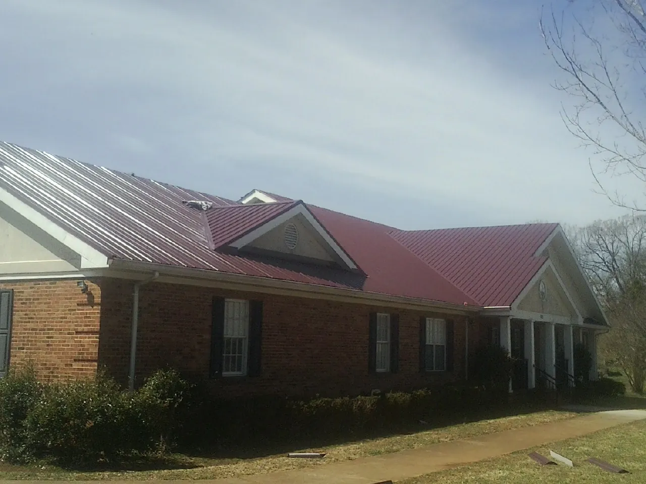 Red metal roof with gabled entries on a long brick building, from a Hail Damage Roof Repair job in Burnt Hills