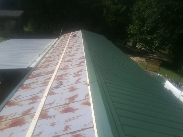Old rusted panels beside newly installed green metal roofing — Wind Damage Roof Repair by Roofing Brothers in Burnt Hills