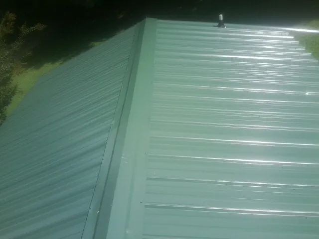 New green metal panels meeting at the ridge of a roof — Flat Roof Repair work by our crew in Burnt Hills
