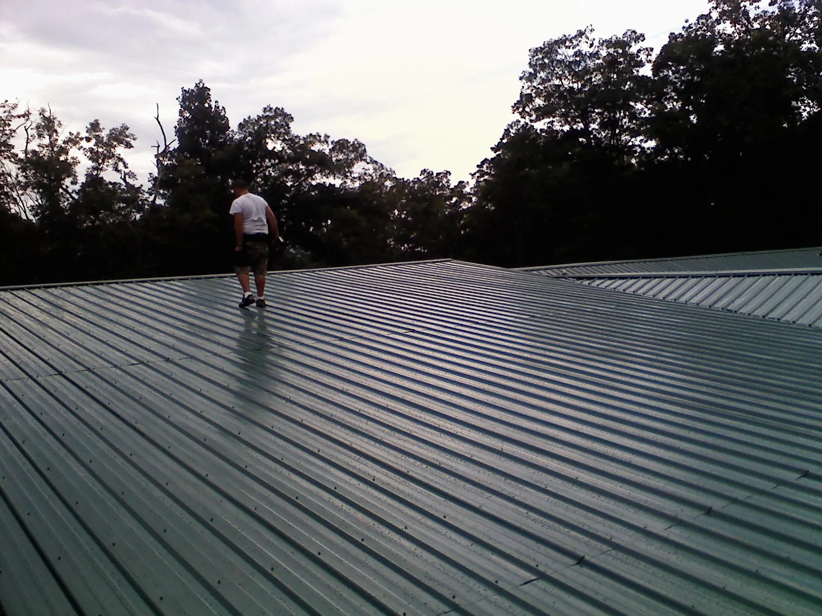 Roofer walking a wide expanse of new green metal roofing in Burnt Hills