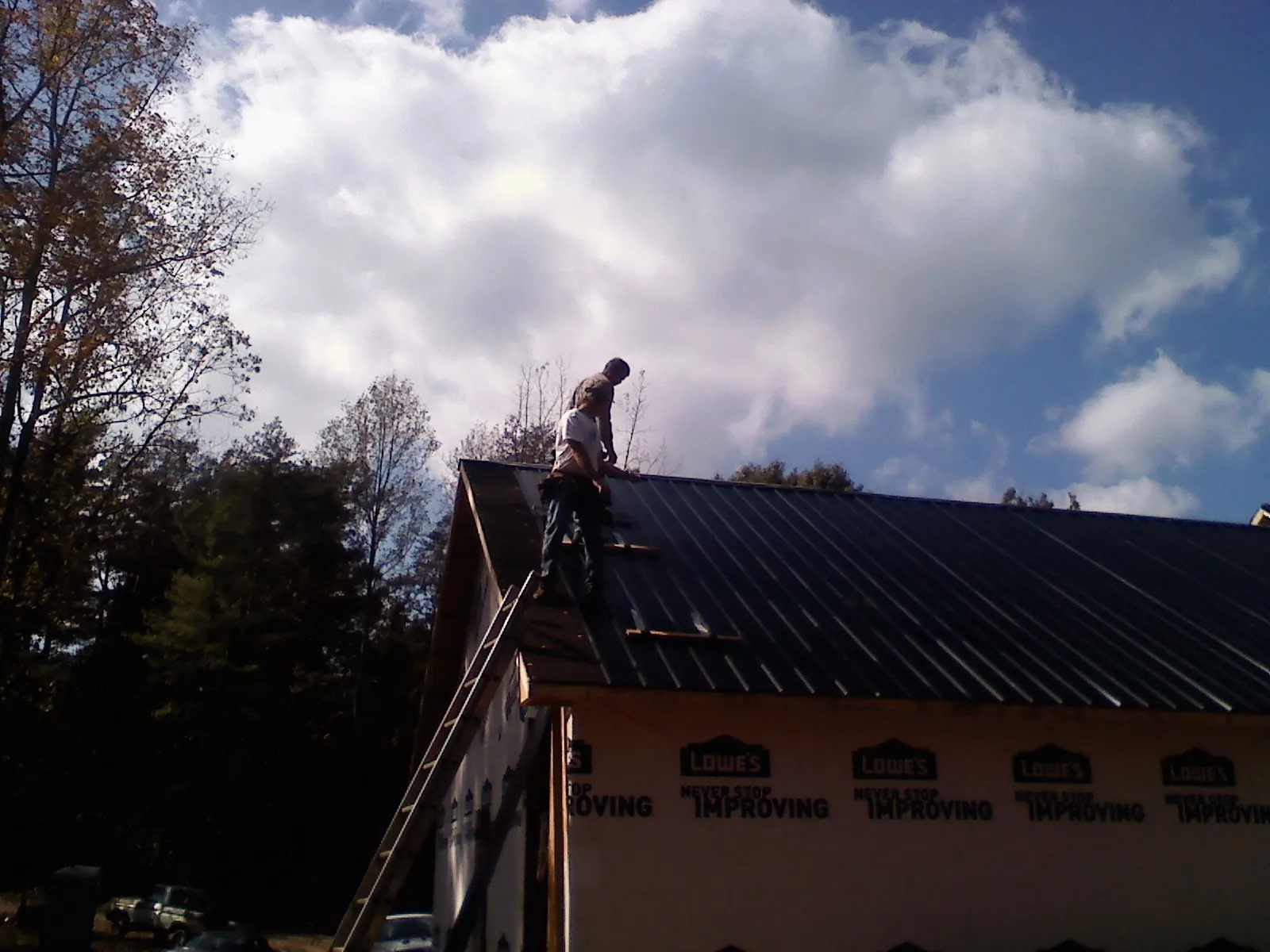 Roofer fastening dark metal panels high against a cloudy sky, from a Roof Inspection job in Burnt Hills
