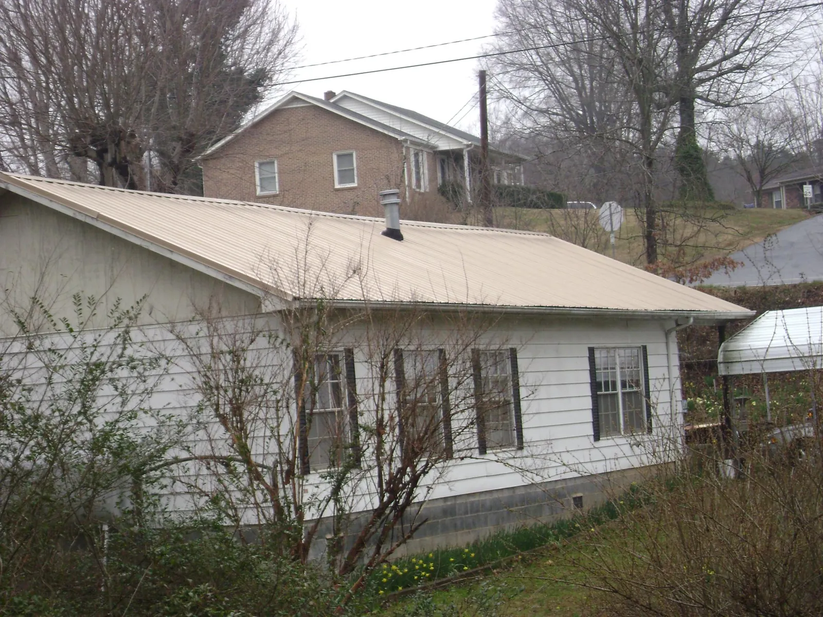 Tan metal roof on a white sided house set into a hillside — Commercial Roofing by Roofing Brothers in Burnt Hills