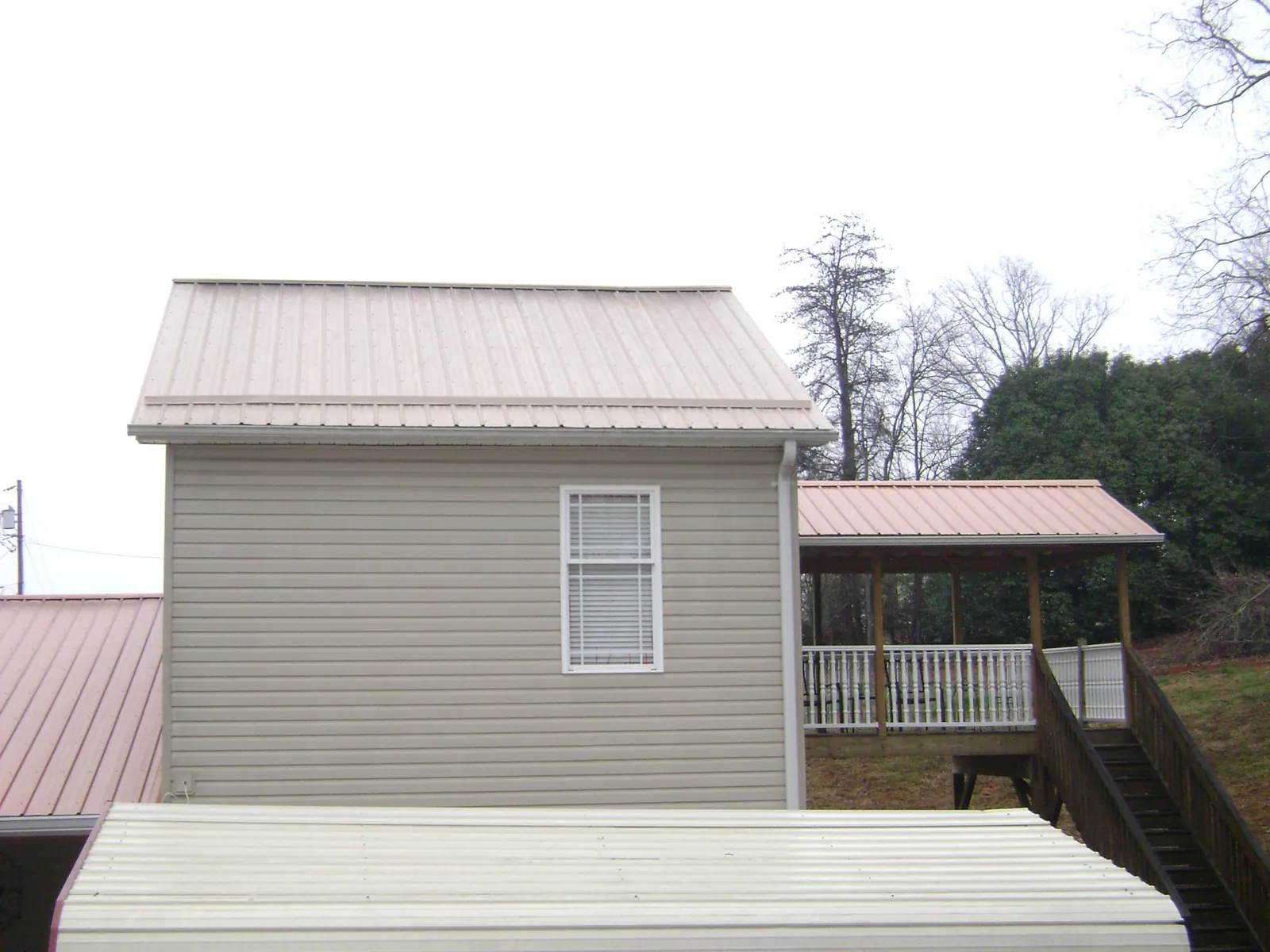 Tan metal roofs on a two story addition and attached porch, from a Roof Replacement job in Burnt Hills
