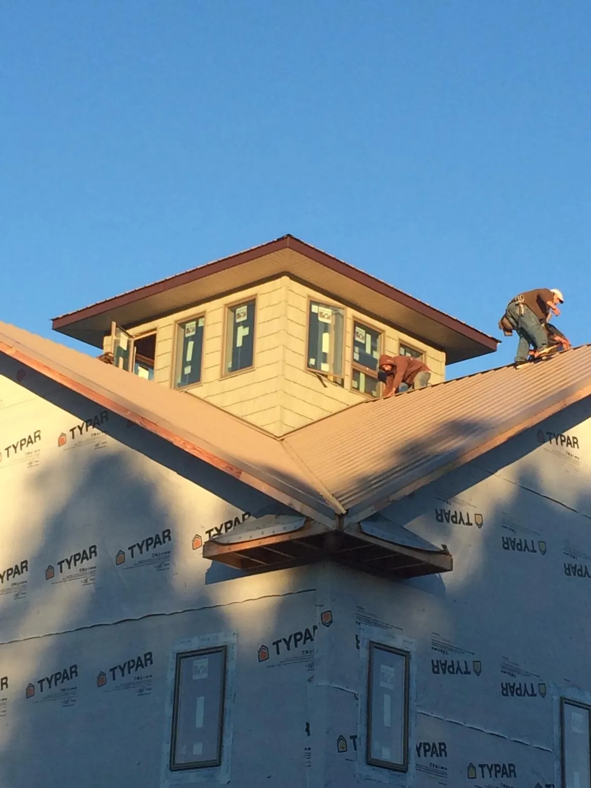 Roofers working around a rooftop cupola on a new metal roof at sunset — Roof Waterproofing in Burnt Hills by Roofing Brothers